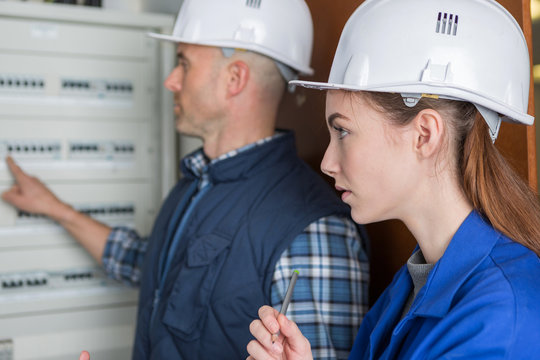 woman and teacher measuring electrical current of a fuse board