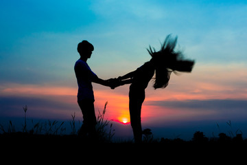 silhouette of romantic couple at the sunset time on meadow. Have a beauty pink and blue sky.