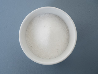 Close up of homemade vanilla sugar made from white caster sugar and a vanilla bean pod in small white bowl on blue background