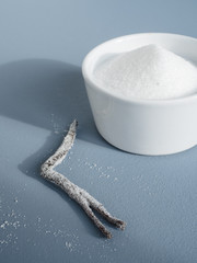 Close up of homemade vanilla sugar made from white caster sugar and a vanilla bean pod in small white bowl on blue background
