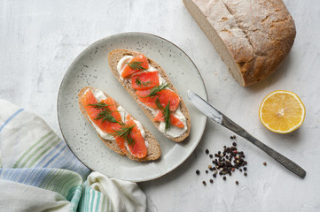 Toast with smoked salmon, cream cheese and dill on rustic plate. White concrete table. Natural...