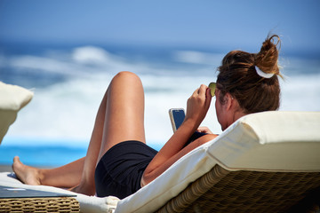atractiva y joven mujer tomando sol y viendo el celular