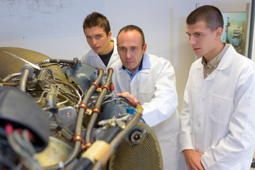 Tutor with apprentices, looking at mechanical object