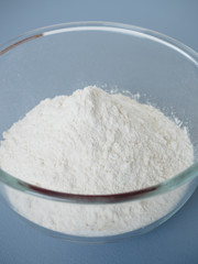 Close up shot of pile of plain white wheat flour in glass mixing bowl prepared for baking on blue background
