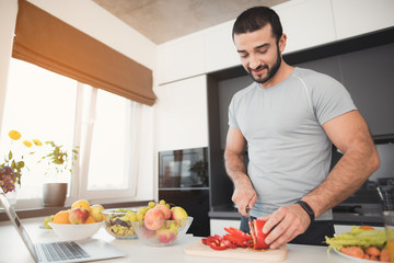 A young athletic man prepares a delicious salad of vegetables. He cuts the vegetables.