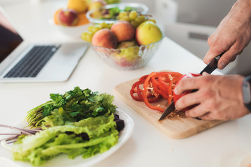 Close up. A young athletic man prepares a delicious salad of vegetables. He cuts the vegetables.