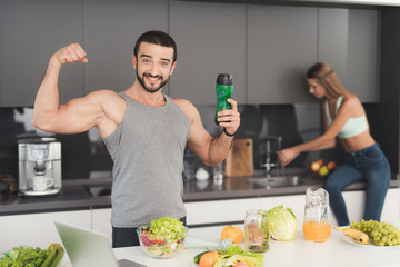 A man and a woman in the kitchen in the morning. A man will play with a green vegetable cocktail in his hands.