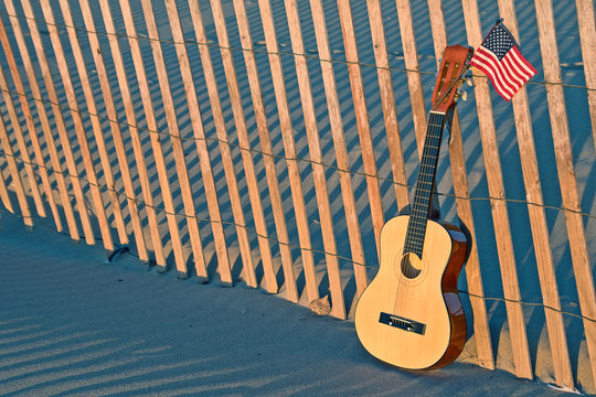 six string guitar with American flag in sand on beach fence