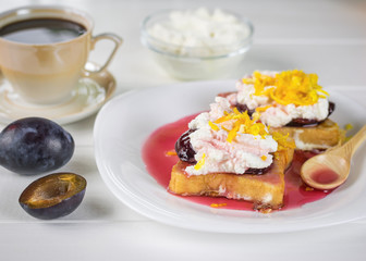 Breakfast of French bread with curd cream, plum jam and orange zest on a white table.