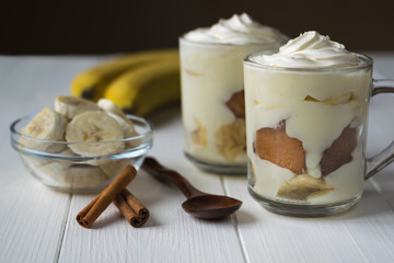 Two cups with banana pudding, banana slices and cinnamon on a white wooden table.