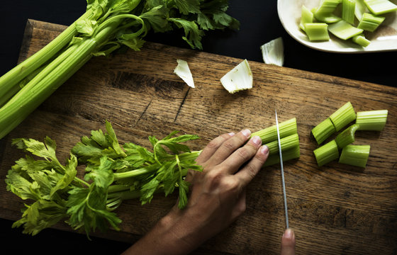 Aerial view of hands with knife cutting celery on wooden cut board