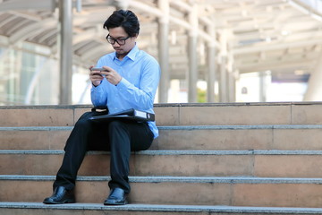 Soft focus of handsome young Asian business man in blue shirt looking mobile smart phone at outside office