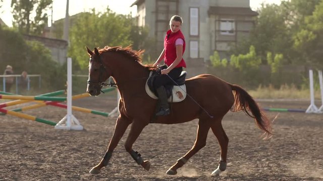 Professional female jockey rides on horseback. Slow motion. Young girl is riding on a beautiful brown horse.