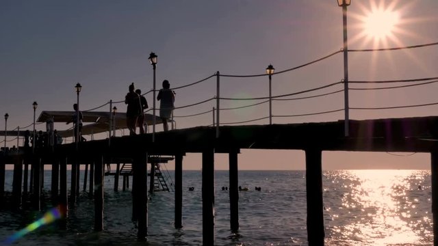 People walk along the pier, bridge. Sunset at the sea.