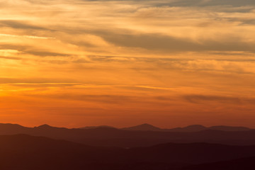 A silhouette of a mountain peak at sunset, under a big sky with beautiful red and yellow clouds