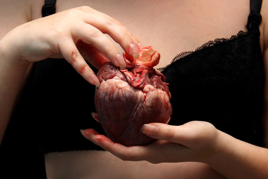 real human heart in beautiful female hands. symbol of love, pain. Insidious nude girl in a bra black with heart of man. Feminism or patriarchy. postcard st Valentine's Day. Love causing pain. Low key