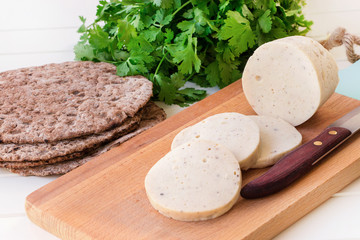 Dietary homemade boiled sausage mortadella from chicken breast with spices on a wooden cutting board. Protein rye multicereal flatbread.