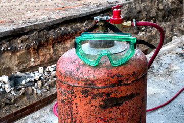 Red rusty gas cylinder standing on the pavement with a green diving mask.
