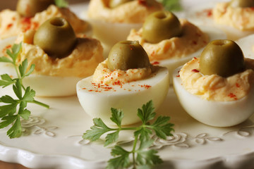 Spicy deviled eggs garnished with green olives on white plate