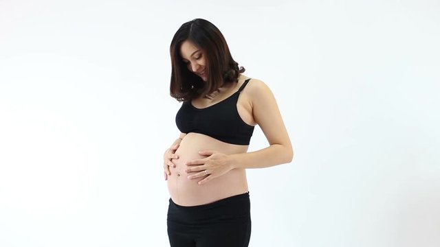 Pregnant woman holding belly, playing with her baby and smiling over white background