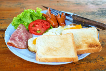 Morning breakfast with sausage, bacon, eggs and toast on wooden table, American food style