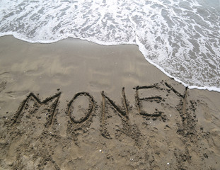 text MONEY written on the sand and the wave that is erasing the