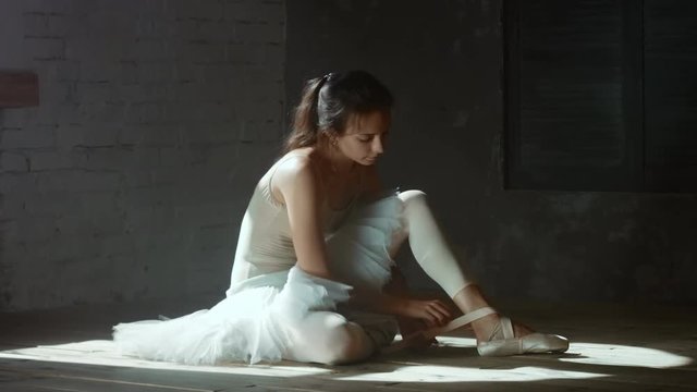 Ballet dancer sitting on the floor and dressing up pointe shoes