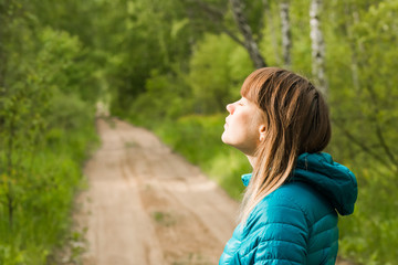 A young pretty woman enjoying the first rays of the spring sun on a picturesque path in a deciduous forest