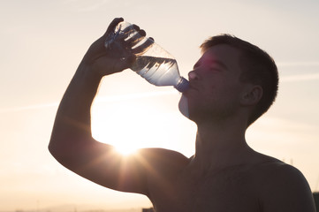 Topless man drinking water at beach