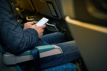 Man hand holding smartphone on board for chat and planning the trip. Male traveller using smartphone sufing the internet and chat during flight.