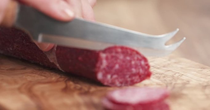Slow motion closeup female slicing thin fuet sausage