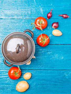 Picture from above of iron pot, tomato, potato, onion on blue wooden background