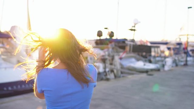 Woman in sunglasses walking along the dock with a lot of yachts and boats at sunset, close up. Slow motion