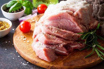 Pork fillet on a cutting board, raw meat, cherry tomatoes and various spices on a stone or slate background.