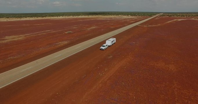 Four Wheel Drive vehicle and Caravan parked next to a long straight highway in the outback of Western Australia surrounded by pink wildflowers.