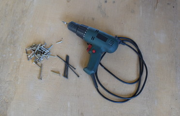 Electric screwdriver and self-tapping screws of different sizes on a sheet of old plywood.