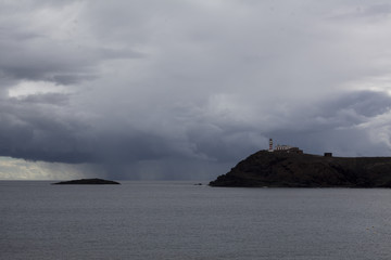 Coast with a lighthouse standing on a black rock. Dark rain clouds in the sky