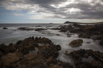 Fototapeta na wymiar Rough coast with water running through the rocks. Dark clouds in the sky.