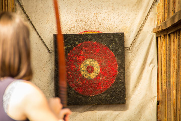 A girl shoots from a red wooden bow with wooden arrows on a wooden multicolored target.