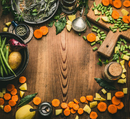 Obraz na płótnie Canvas Healthy clean cooking and eating concept. Kitchen table from above with various ingredients: chopped vegetables, herbs and spices, cutting board and spoon, frame, top view