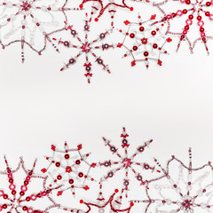 Christmas or winter concept. Frame of various handmade red snowflakes made from beads and bugle on white desk background, top view. Layout for greeting card and winter holidays
