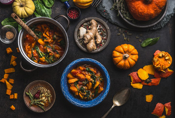 Vegan pumpkin stew dish with spinach served in bowl with spoon on dark kitchen table background...