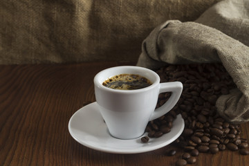 a small cup of hot coffee on a table with coffee beans