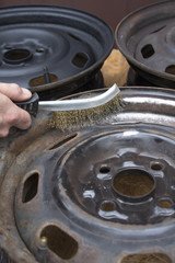 Mechanik czyści stalową felgę samochodową ręcznie za pomocą drucianej szczotki.