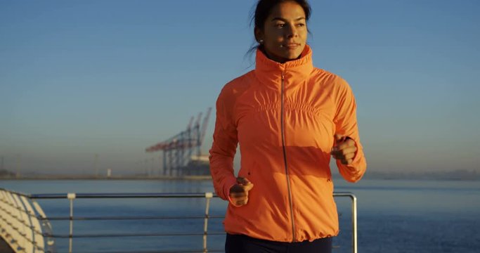 Portrait shot of young sporty attractive woman runner in yellow coat jogging and getting away on the sea dock .The blue skied and sunny weather. Outdoor