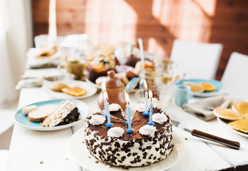 Birthday cake decorated by burning candles, chocolate glaze and sprinkles and whipped cream swirls