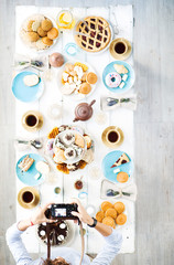 Woman shooting served table with cups of tea and homemade desserts