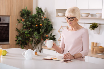 Cheerful aged woman making notes in the kitchen