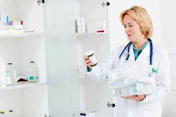 Female doctor looking through various pill-bottles and other medicine from plastic container