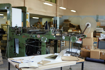Workplace of technical worker with laptop and notepads on background of factory equipment